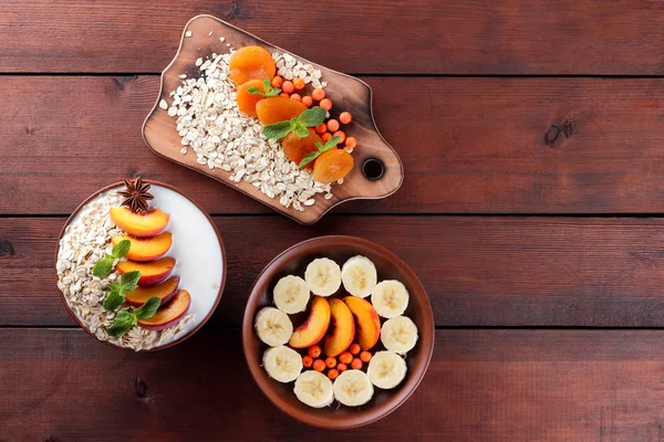 Oatmeal with fruits and green mint. Oat flakes with milk and dried apricots on wooden background. Healthy food for vegans. Dry oats with peaches, anise and berries of mountain ash. Copy space