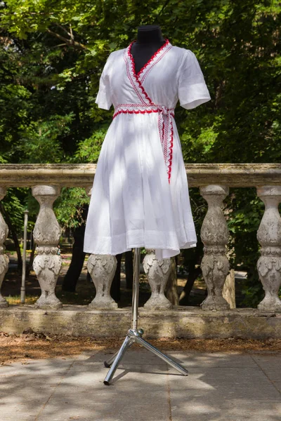 White dressing on mannequin. White dress made of natural fabric with red elements. Custom tailoring. Women's summer cotton dress with belt