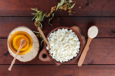 Süzme peynir ve krem. Yumuşak peynir ve bal ahşap kurullarında. Çanak çömlek ve ıhlamur çiçek süzme peynir. Ahşap arka plan üzerinde sicim. Tahta kaşık krem. Ahşap stand tatlım. Kopya alanı