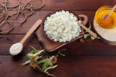 Süzme peynir ve krem. Yumuşak peynir ve bal ahşap kurullarında. Çanak çömlek ve ıhlamur çiçek süzme peynir. Ahşap arka plan üzerinde sicim. Tahta kaşık krem. Ahşap stand tatlım. Kopya alanı