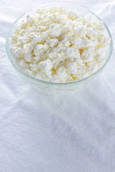 Cottage cheese. Cottage cheese on white background. Soft cheese in glassware on white napkin. Dairy product for breakfast. Copy space