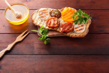 Izgara sebze ile tost. Vejetaryen yiyecekler. Kırmızı ve sarı domates. Domates, soğan ve otlar ile ızgara sandviç. Sebze ve ballı ekmek. Vegan tost ahşap tahta üzerinde
