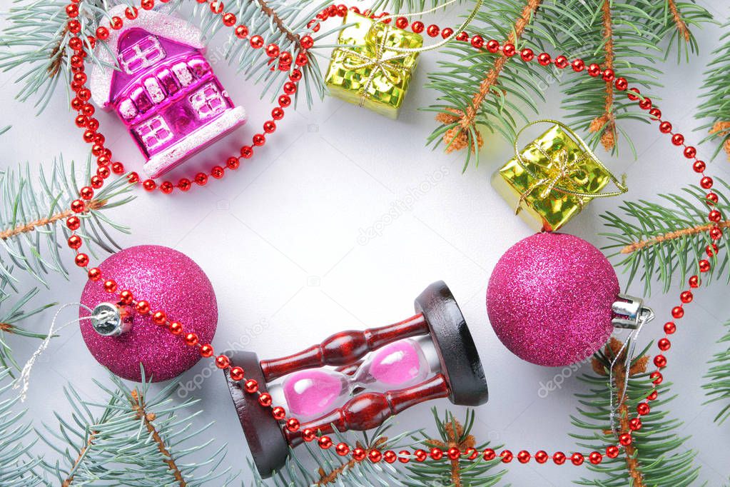 Christmas decorations and hourglass. Spruce branches and holiday decorations on white background. Pink balls and toy house. Red necklace and golden boxes for festive Christmas tree