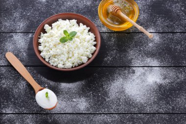 Kil kase ve ahşap kurullarında bal süzme peynir. Tahta kaşık ekşi krema. Süt ürünleri ve bal koyu arka plan üzerinde. Taze nane ve kahvaltı için yumuşak peynir