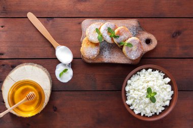 Krep peynir ile pudra şekeri serpilir. Cheesecakes ahşap tahta üzerinde. Kil kase ve tahta kaşık krem peynir. Bal ve süt ürünleri. Kopya alanı