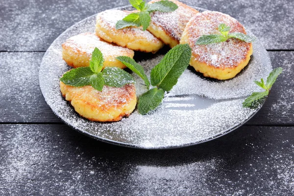 Cottage cheese pancakes with fresh mint sprinkled with powdered sugar. Syrniki on dark wooden boards. Healthy food for breakfast. Dish of milk products. Copy space