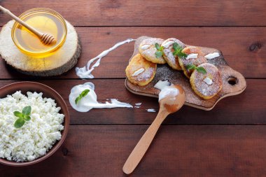 Süzme peynir krep ile pudra şekeri serpilir. Cheesecakes ahşap tahta üzerinde. Kil kase ve tahta kaşık krem peynir. Bal ve süt ürünleri. Kopya alanı