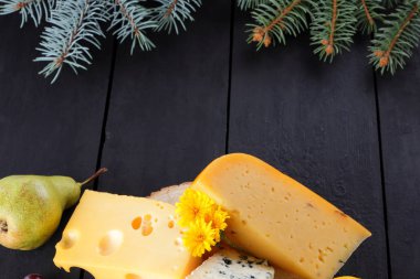 Peynir ve meyve karanlık panoları ve Noel ağacı dalları üzerinde çeşitli türleri. İsviçre peyniri, dorblu, Flamanca peynir Noel için. Süt ve süt ürünleri, limon, üzüm, armut. Üstten görünüm