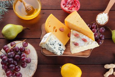 Çeşitli tür peynir meyve ve ahşap kurullarında tatlım. Noel ağacı dalı. İsviçre peyniri, mavi peynir, camembert ve süzme peynir. Süt ve süt ürünleri, limon, üzüm, armut ve nar