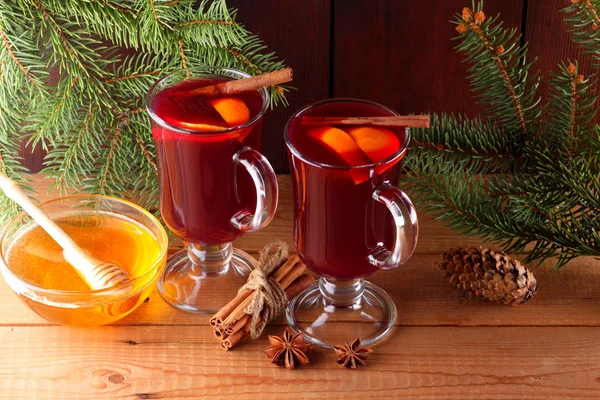 Mulled wine and Christmas tree branches on wooden boards. Christmas mulled wine, cinnamon sticks, anise and honey. Alcoholic drink of wine, fruit and honey. Festive drink on wooden boards