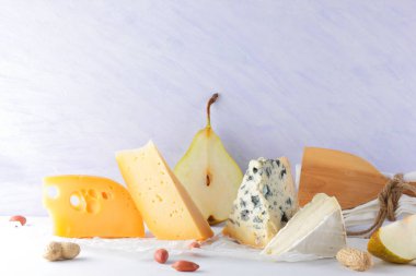 Çeşitli peynirler, armut ve beyaz zemin üzerine fıstık. Mavi peynir ve camembert parşömen kağıt üzerinde. Süt ürünleri ve meyveler kahvaltıda. Sağlıklı gıda