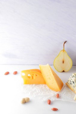 Çeşitli peynirler, armut ve beyaz zemin üzerine fıstık. Mavi peynir ve camembert parşömen kağıt üzerinde. Süt ürünleri ve meyveler kahvaltıda. Sağlıklı gıda