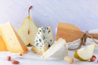 Çeşitli peynirler, armut ve beyaz zemin üzerine fıstık. Mavi peynir ve camembert parşömen kağıt üzerinde. Süt ürünleri ve meyveler kahvaltıda. Sağlıklı gıda