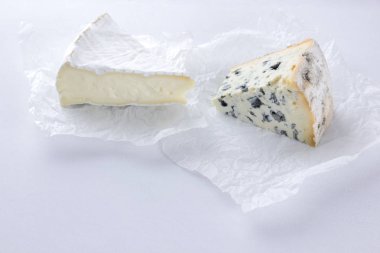 Camembert ve mavi peynir parşömen kağıt üzerinde. Beyaz arka plan üzerinde çeşitli peynir parçalarını. Dorblu ve yumuşak peynir minimalizm tarzı. Çevre dostu süt ürünleri. Kopya alanı