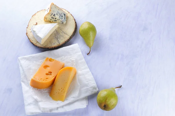 Camembert, yellow cheese and blue cheese on wooden board. Pieces of various cheeses and pears on white napkin. Dorblu and soft cheese in style of minimalism. Cheese and fruits on white background