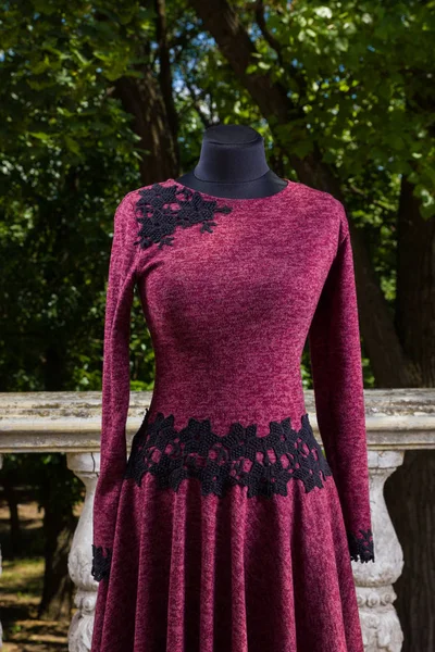 Autumn burgundy dress with embroidery. Women\'s dress with long sleeve on mannequin. Women\'s clothing individual tailoring. Dress on background of green trees
