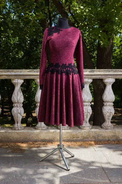 Autumn burgundy dress with embroidery. Women\'s dress with long sleeve on mannequin. Women\'s clothing individual tailoring. Dress on background of green trees