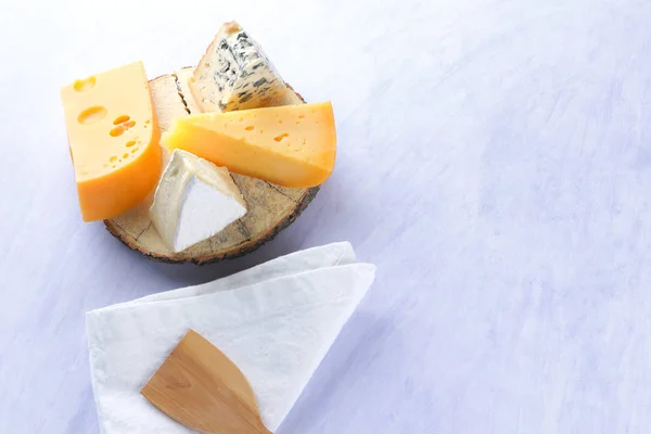 Camembert, hard yellow cheese and blue cheese on wooden board. Pieces of various cheeses on white napkin. Dorblu and soft cheese in style of minimalism. Dairy products