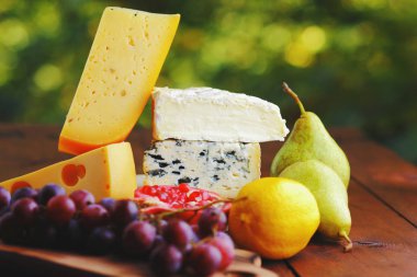 Camembert, brie, sert peynir ve üzüm bir ahşap stand. Adet farklı peynir, armut ve limon üzerinde arka plan bulanık. Dorblu, yumuşak peynir ve nar kurullarında. Peynir ve meyve