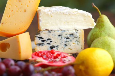 Camembert, brie, sert peynir ve üzüm bir ahşap stand. Adet farklı peynir, armut ve limon üzerinde arka plan bulanık. Dorblu, yumuşak peynir ve nar kurullarında. Peynir ve meyve