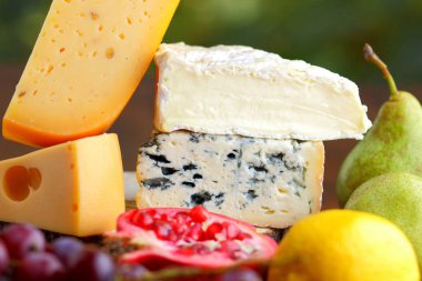 Camembert, brie, sert peynir ve üzüm bir ahşap stand. Adet farklı peynir, armut ve limon üzerinde arka plan bulanık. Dorblu, yumuşak peynir ve nar kurullarında. Peynir ve meyve