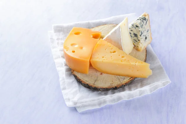 Camembert, hard yellow cheese and blue cheese on wooden board. Pieces of various cheeses on white napkin. Dorblu and soft cheese in style of minimalism. Dairy products