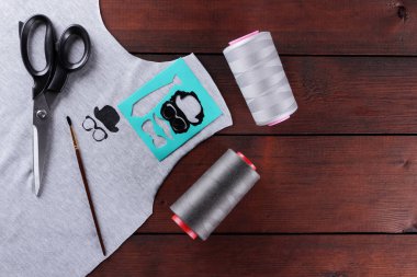 Dikiş çocuk el yapımı t-shirtler. Gri kumaş ve ahşap kurullarında gri konu. Terzilik işlemi: gri kumaş, makas, konu, püskül ve siyah boya. T-shirt boş