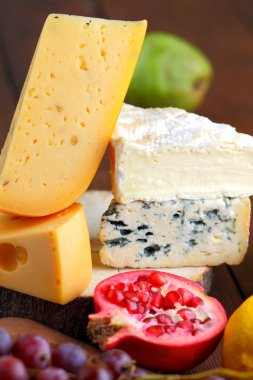 Camembert, brie, sert peynir ve üzüm bir ahşap stand. Adet farklı peynir, armut ve limon üzerinde arka plan bulanık. Dorblu, yumuşak peynir ve nar kurullarında. Peynir ve meyve