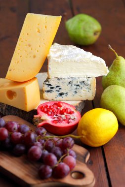 Camembert, brie, sert peynir ve üzüm bir ahşap stand. Adet farklı peynir, armut ve limon üzerinde arka plan bulanık. Dorblu, yumuşak peynir ve nar kurullarında. Peynir ve meyve