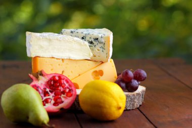 Camembert, brie, sert peynir ve üzüm bir ahşap stand. Adet farklı peynir, armut ve limon üzerinde arka plan bulanık. Dorblu, yumuşak peynir ve nar kurullarında. Peynir ve meyve