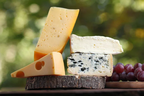 在木板上的寒台 硬奶酪和蓝色奶酪 在模糊的背景下的各种奶酪和葡萄片 在木板上的多布布和软奶酪 Bokeh 上的奶酪和葡萄 — 图库照片