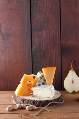 Peynir, armut ve ahşap kurullarında fıstık türleri. Camembert, sert sarı peynir, ahşap arka plan üzerinde dorblu. Süt ürünleri, yarım armut ve fındık