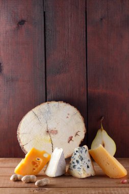 Peynir, armut ve ahşap kurullarında fıstık türleri. Camembert, sert sarı peynir, ahşap arka plan üzerinde dorblu. Süt ürünleri, yarım armut ve fındık