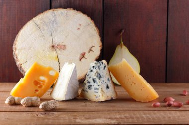 Peynir, armut ve ahşap kurullarında fıstık türleri. Camembert, sert sarı peynir, ahşap arka plan üzerinde dorblu. Süt ürünleri, yarım armut ve fındık