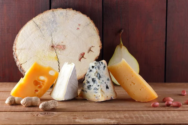 Peynir, armut ve ahşap kurullarında fıstık türleri. Camembert, sert sarı peynir, ahşap arka plan üzerinde dorblu. Süt ürünleri, yarım armut ve fındık