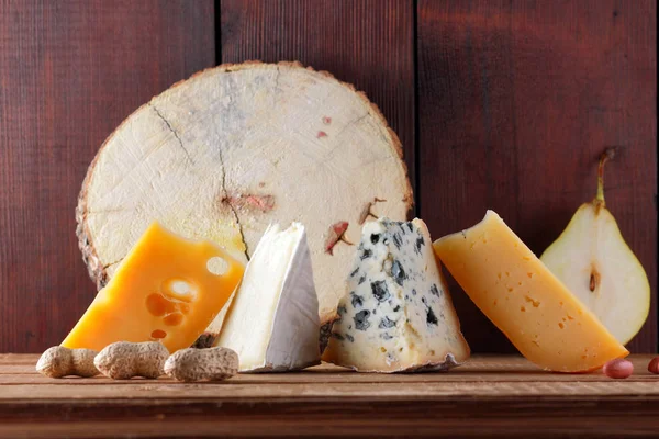 Peynir, armut ve ahşap kurullarında fıstık türleri. Camembert, sert sarı peynir, ahşap arka plan üzerinde dorblu. Süt ürünleri, yarım armut ve fındık