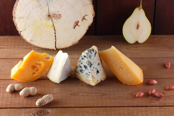 Various types of cheese, pear and peanuts on wooden boards. Camembert, hard yellow cheese, dorblu on a wooden background. Dairy products, half pears and nuts