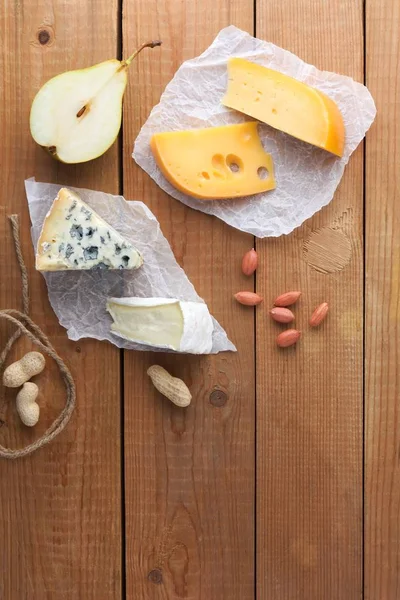 Peynir, armut ve parşömen kağıt üzerine fıstık ürün yelpazesine. Camembert, sert sarı peynir, dorblu ahşap kurullarında. Süt ürünleri, yarım armut ve fındık