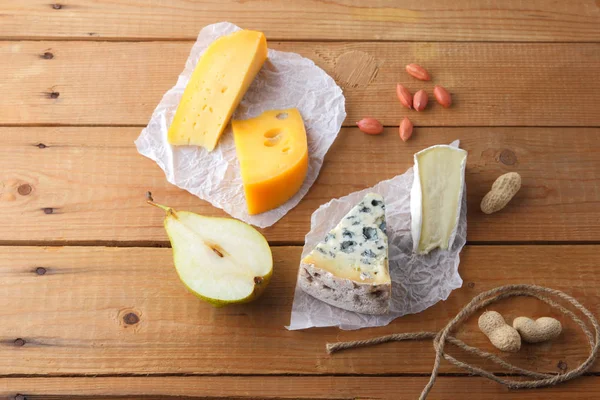 Peynir, armut ve parşömen kağıt üzerine fıstık ürün yelpazesine. Camembert, sert sarı peynir, dorblu ahşap kurullarında. Süt ürünleri, yarım armut ve fındık