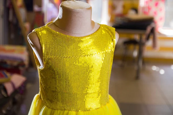 Yellow children\'s dress with sparkles on mannequin. Little yellow dress in studio. Sewing women\'s handmade children\'s clothing. Yellow baby clothes