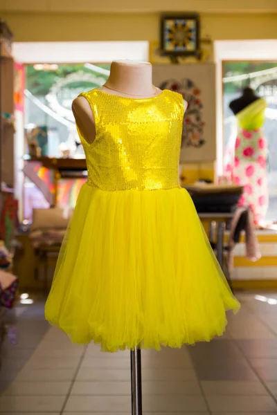 Yellow children's dress with sparkles on mannequin. Little yellow dress in studio. Sewing women's handmade children's clothing. Yellow baby clothes