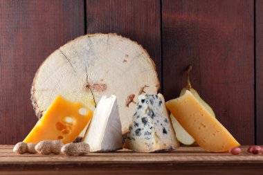Peynir, armut ve ahşap kurullarında fıstık türleri. Camembert, sert sarı peynir, ahşap arka plan üzerinde dorblu. Süt ürünleri, yarım armut ve fındık