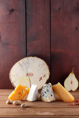 Peynir, armut ve ahşap kurullarında fıstık türleri. Camembert, sert sarı peynir, ahşap arka plan üzerinde dorblu. Süt ürünleri, yarım armut ve fındık