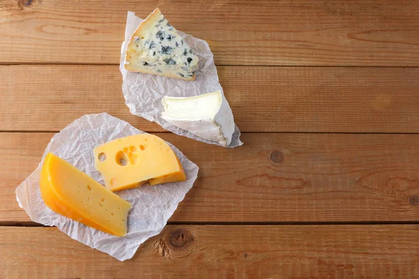 Cheese on wooden boards. Camembert, hard yellow cheese, dorblu on parchment paper. Top view