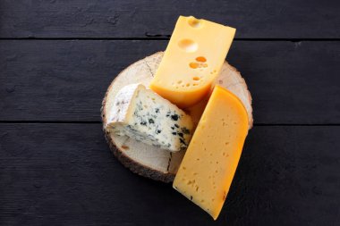 Sert peynir ve mavi peynir bir ahşap stand. Peynir siyah kurullarında farklı türleri. İsviçre peyniri ve karanlık bir arka plan üzerinde dorblu. Kopya alanı