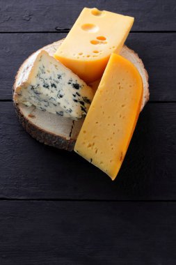 Sert peynir ve mavi peynir bir ahşap stand. Peynir siyah kurullarında farklı türleri. İsviçre peyniri ve karanlık bir arka plan üzerinde dorblu. Kopya alanı