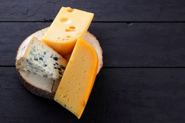 Sert peynir ve mavi peynir bir ahşap stand. Peynir siyah kurullarında farklı türleri. İsviçre peyniri ve karanlık bir arka plan üzerinde dorblu. Kopya alanı