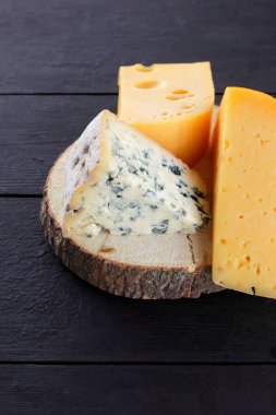 Sert peynir ve mavi peynir bir ahşap stand. Peynir siyah kurullarında farklı türleri. İsviçre peyniri ve karanlık bir arka plan üzerinde dorblu. Kopya alanı