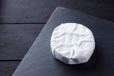 Camembert siyah bir taş gemide. Yumuşak peynir kalıp siyah bir arka plan ile. Minimalizm tarzı kayrak yazı tahtası üzerinde peynir. Kopya alanı