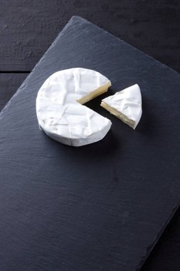 Camembert siyah bir taş gemide. Yumuşak peynir kalıp siyah bir arka plan ile. Minimalizm tarzı kayrak yazı tahtası üzerinde peynir. Kopya alanı